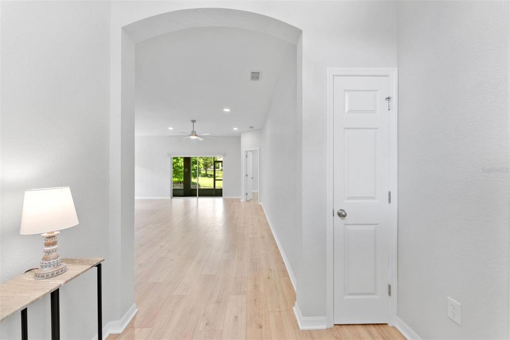 A hallway with light wood flooring leads through an arched doorway into a living area — 6052 CHAMPIONS GATE BOULEVARD, ZEPHYRHILLS, FL