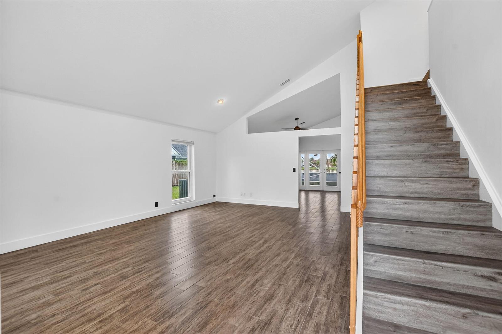 An empty room with wood-look flooring, a vaulted ceiling, and a staircase with wooden railings — 22608 Middletown Drive, Boca Raton FL 33428, BOCA RATON, FL