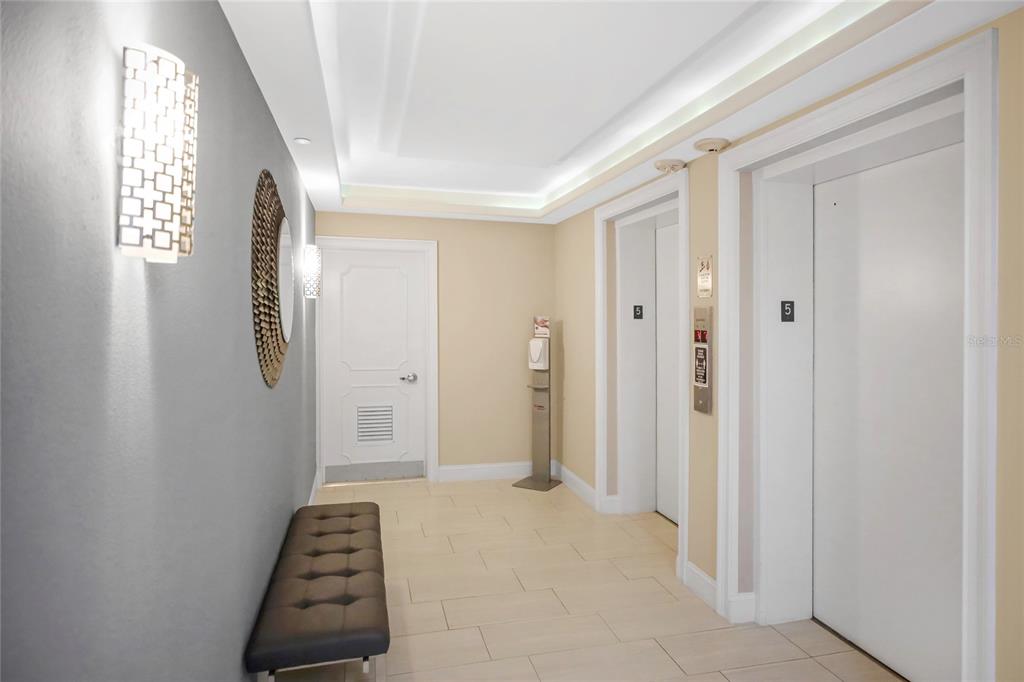 An elevator lobby features two white elevator doors, a bench, and a decorative wall sconce — 1212 BENJAMIN FRANKLIN DRIVE UNIT 504, SARASOTA, FL