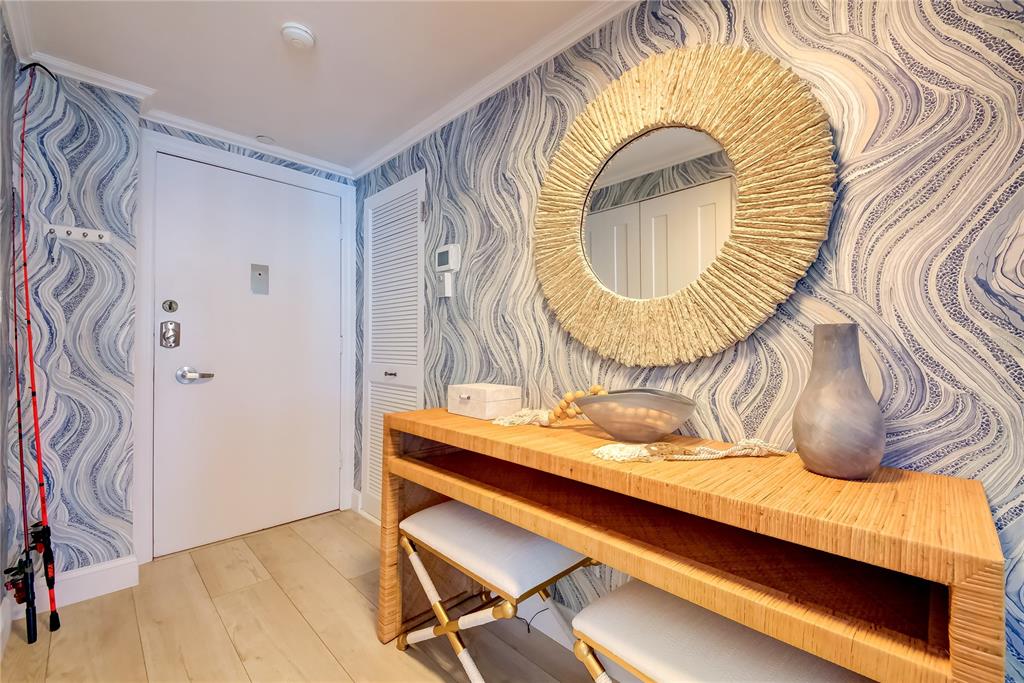 An entryway features blue patterned wallpaper, a round textured mirror, and a wooden console table — 1212 BENJAMIN FRANKLIN DRIVE UNIT 504, SARASOTA, FL