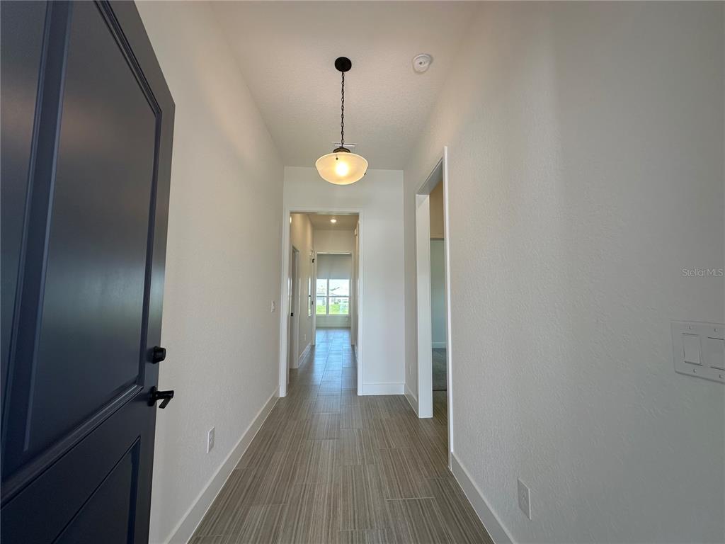 A hallway with light wood-look tile flooring leads toward a windowed room — 12547 NE 48TH TERRACE, OXFORD, FL
