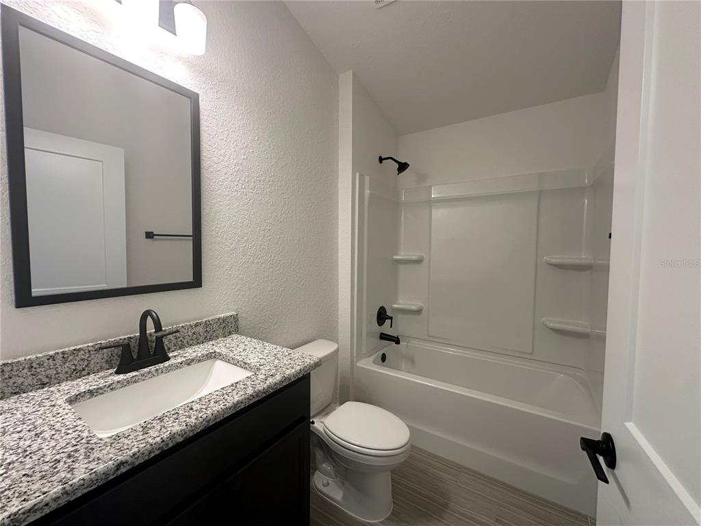 A bathroom features a vanity with a granite countertop, a toilet, and a tub-shower combination — 12547 NE 48TH TERRACE, OXFORD, FL