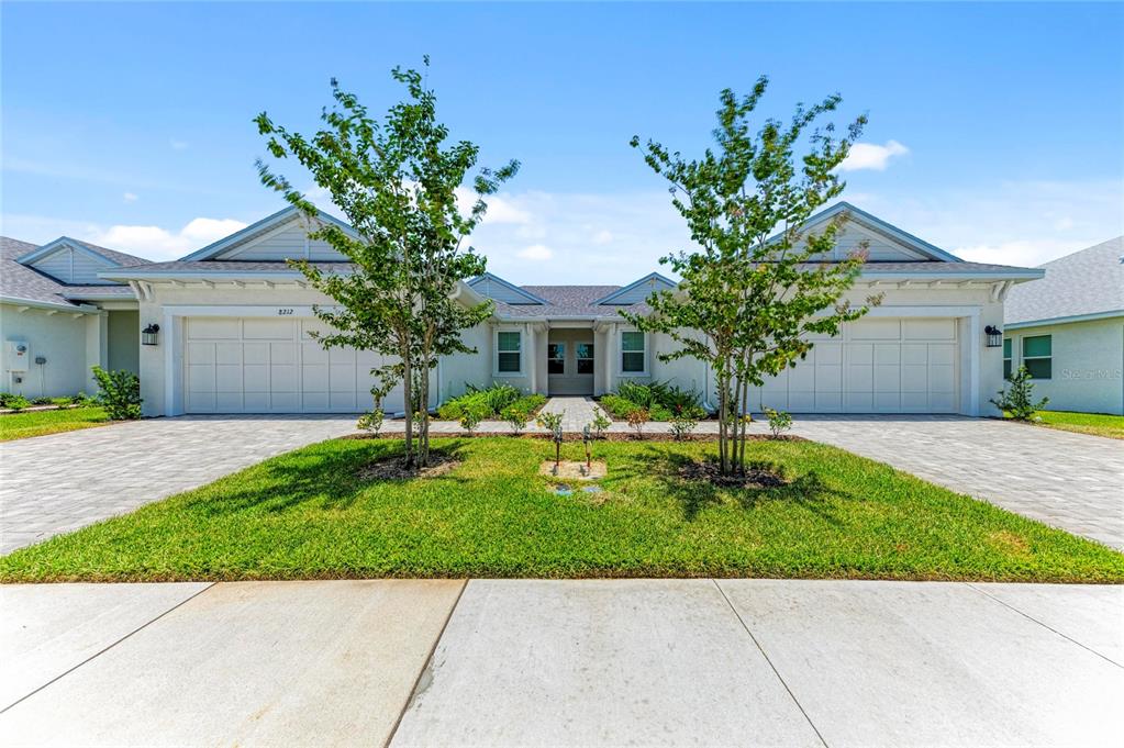 A duplex house features two garage doors, a central entrance, and two trees on a lawn — 8212 CALLAHAN AVENUE, BRADENTON, FL