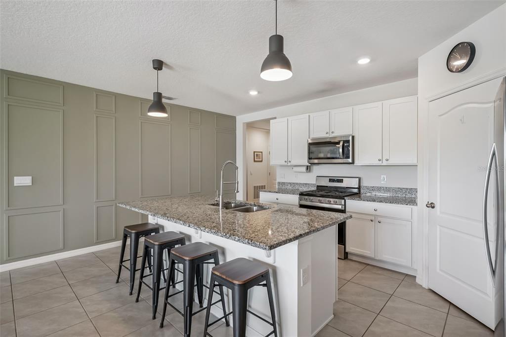 A kitchen features a granite-topped island with bar stools, white cabinetry, and a paneled wall — 623 LAZIO CIRCLE, DEBARY, FL