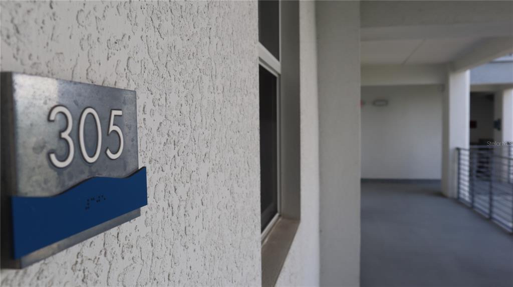 A metal sign with the number 305 is mounted on a textured white exterior wall — 4751 CLOCK TOWER DRIVE UNIT 305, KISSIMMEE, FL