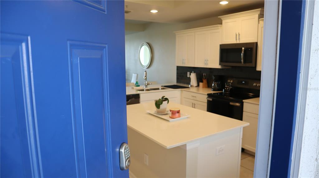 A view through a blue door into a kitchen with white cabinets and an island — 4751 CLOCK TOWER DRIVE UNIT 305, KISSIMMEE, FL