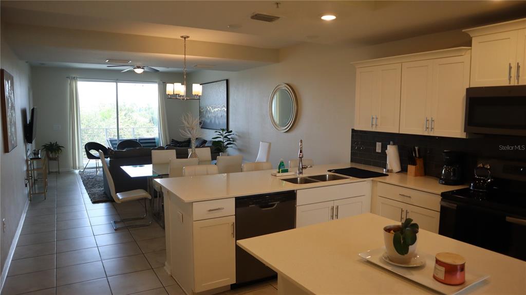 A kitchen with white cabinets and a center island overlooks a dining and living area — 4751 CLOCK TOWER DRIVE UNIT 305, KISSIMMEE, FL