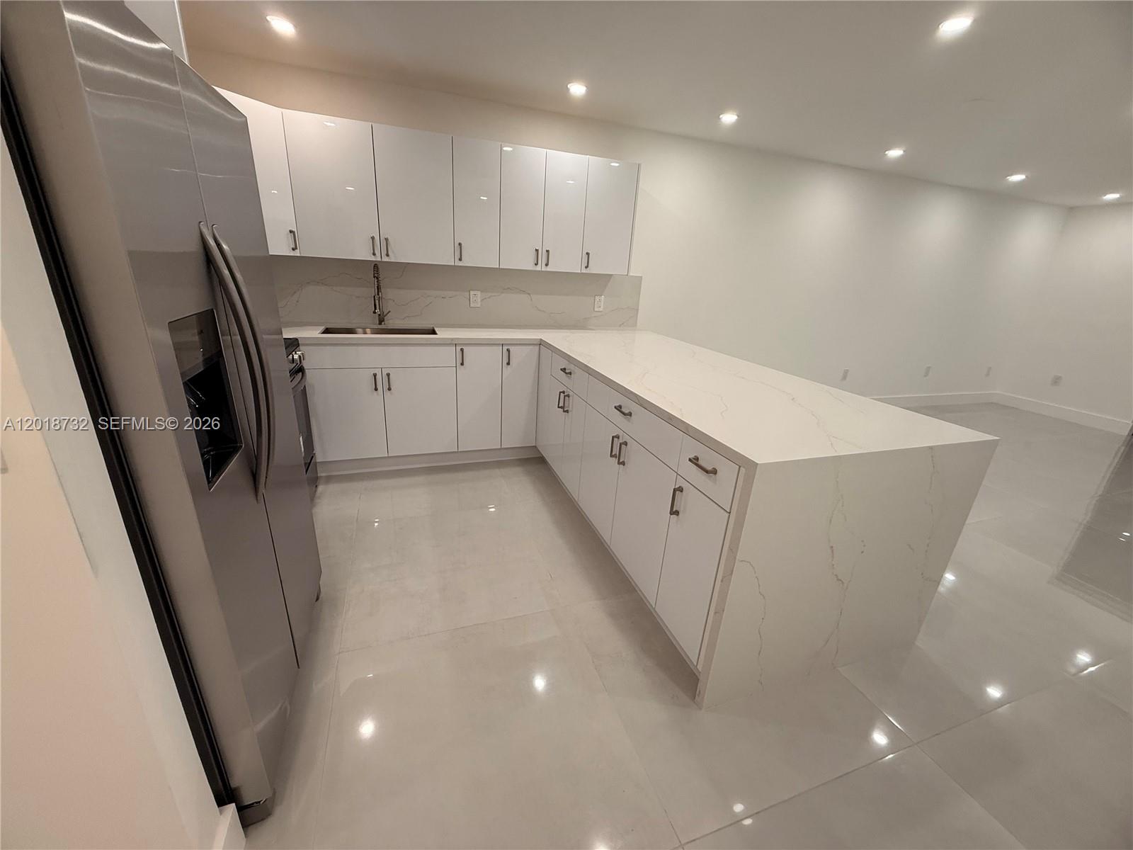 A modern kitchen features white cabinets, stainless steel appliances, and a quartz waterfall island — 6070 W 19th Ave # 315, Hialeah FL 33012, HIALEAH, FL
