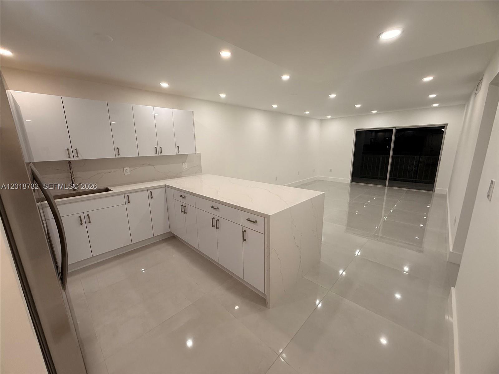 A modern kitchen with white cabinets and a quartz island opens into a spacious living area — 6070 W 19th Ave # 315, Hialeah FL 33012, HIALEAH, FL