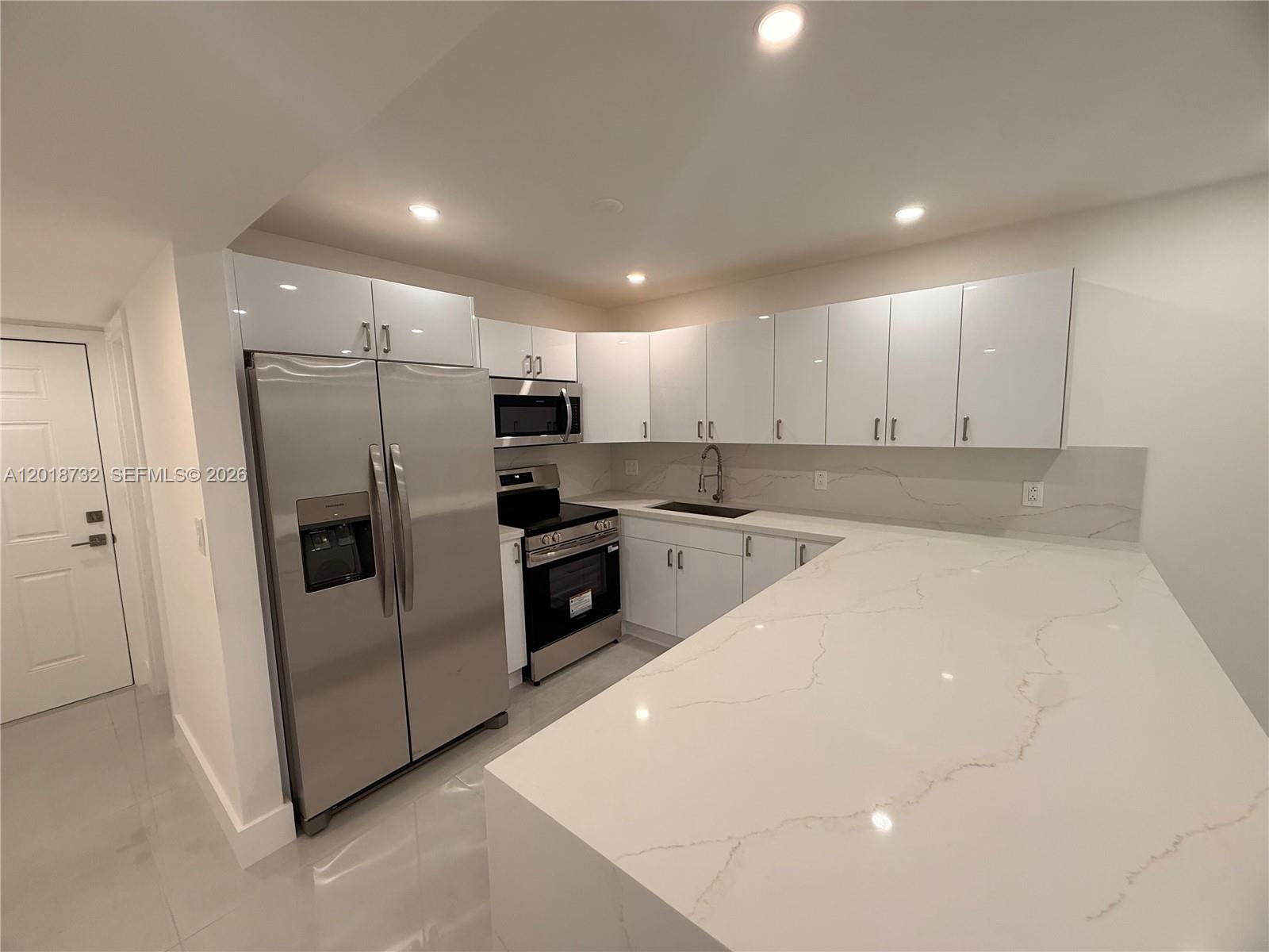 A modern kitchen features white glossy cabinets, stainless steel appliances, and a white marble countertop — 6070 W 19th Ave # 315, Hialeah FL 33012, HIALEAH, FL