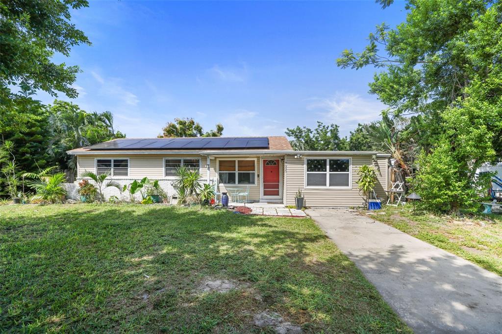 A single-story house with beige siding, a red front door, and solar panels on the roof — 7000 13TH STREET N, ST PETERSBURG, FL
