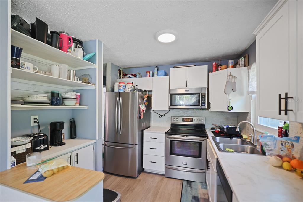 A kitchen features stainless steel appliances, white cabinetry, open shelving, and light-colored countertops — 7000 13TH STREET N, ST PETERSBURG, FL