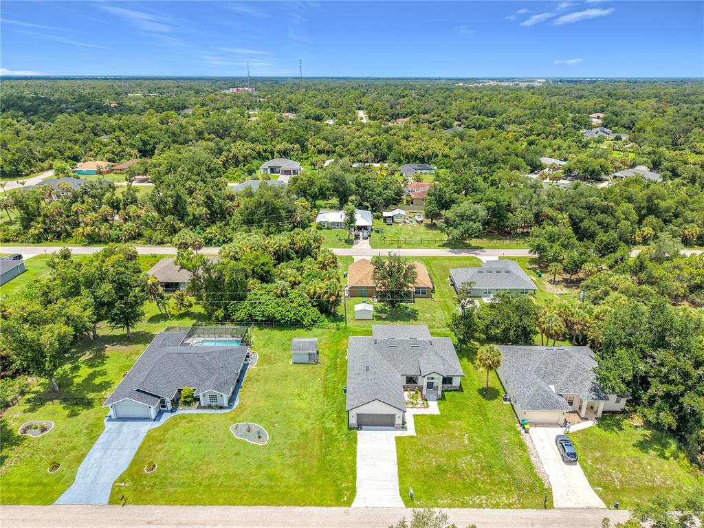 An aerial view shows three suburban houses with driveways and lawns surrounded by dense trees — 275 LECTURN STREET, PORT CHARLOTTE, FL