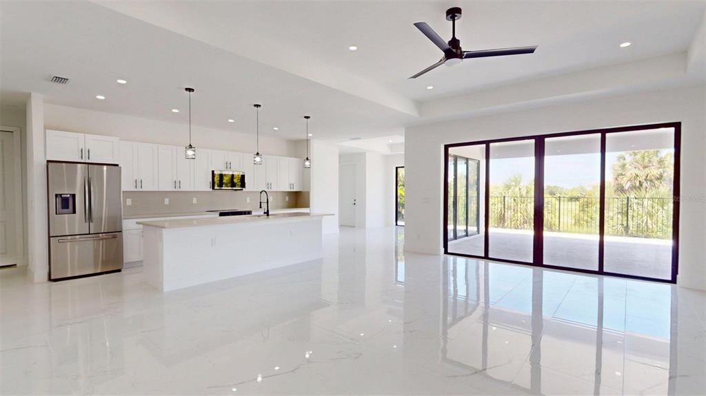 A modern kitchen with white cabinetry and an island opens to a bright living area — 17425 FUEGO LANE, PUNTA GORDA, FL