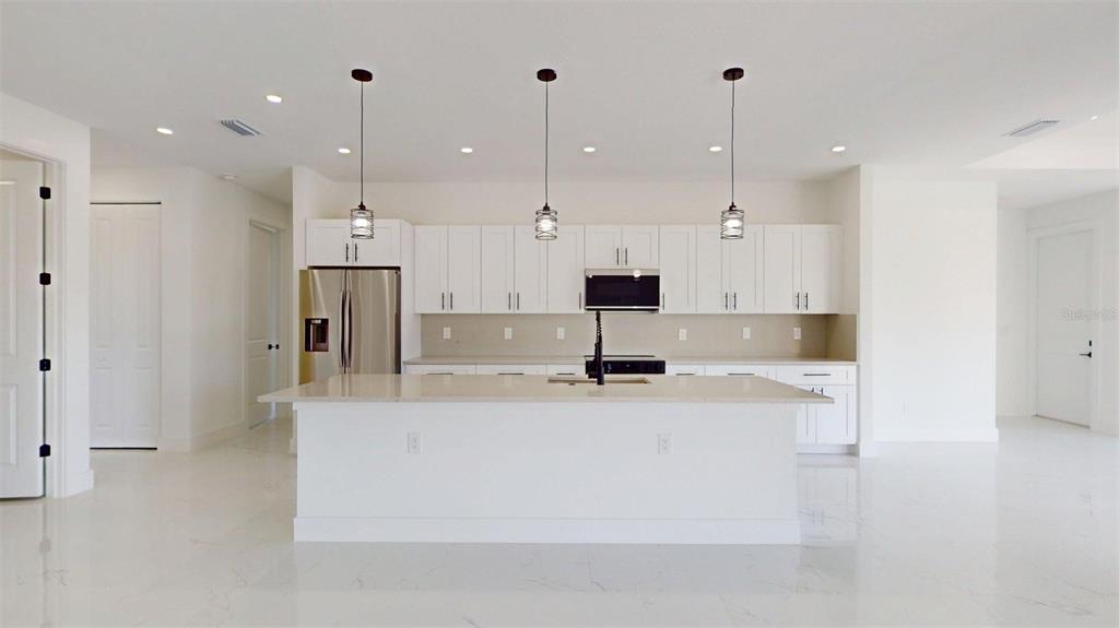 A modern white kitchen features a large island, stainless steel appliances, and three pendant lights — 17425 FUEGO LANE, PUNTA GORDA, FL