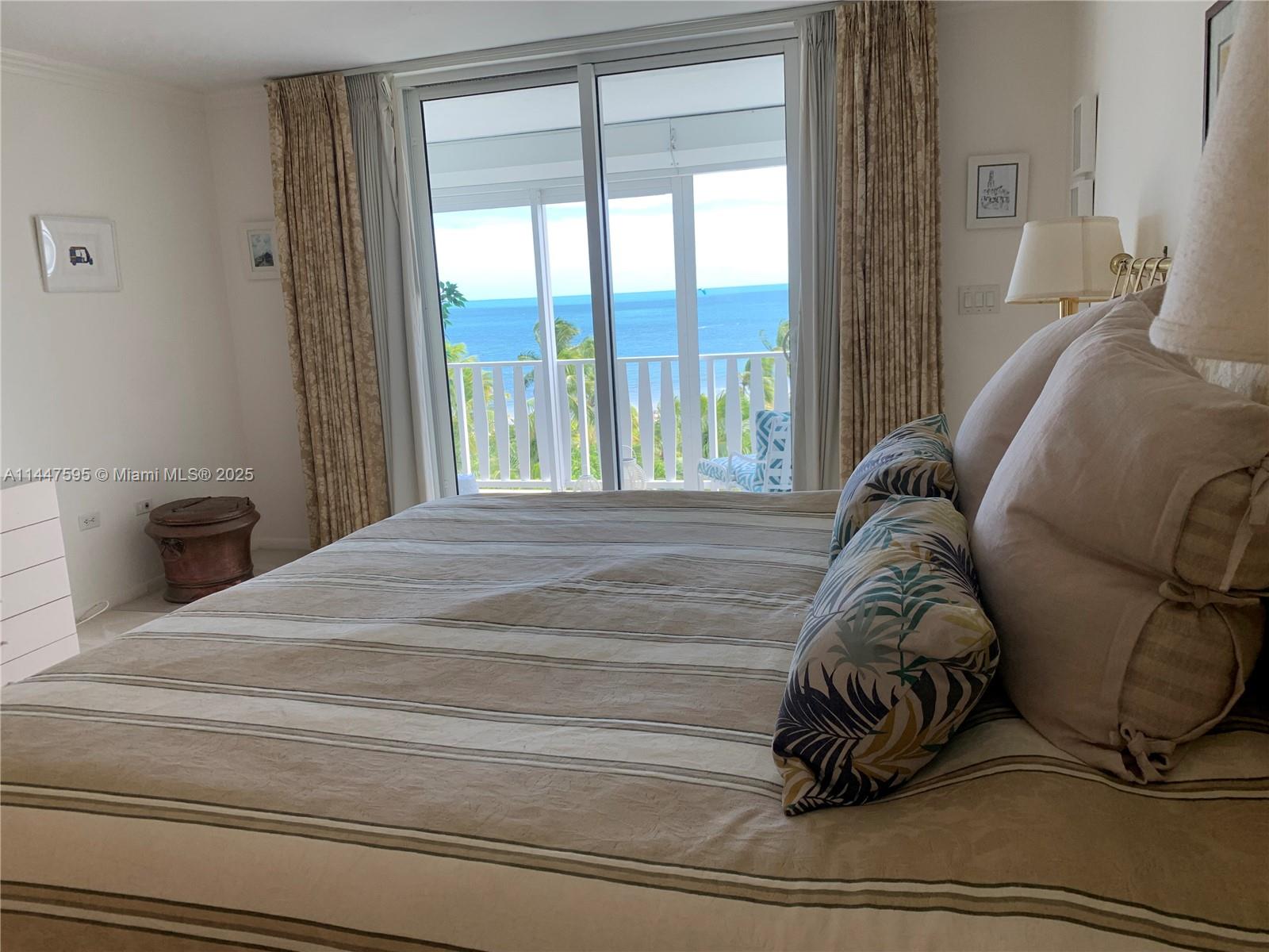 A bedroom features a striped bedspread, a large sliding glass door, and an ocean view — 200 Ocean Lane Dr # 706, Key Biscayne FL 33149, KEY BISCAYNE, FL