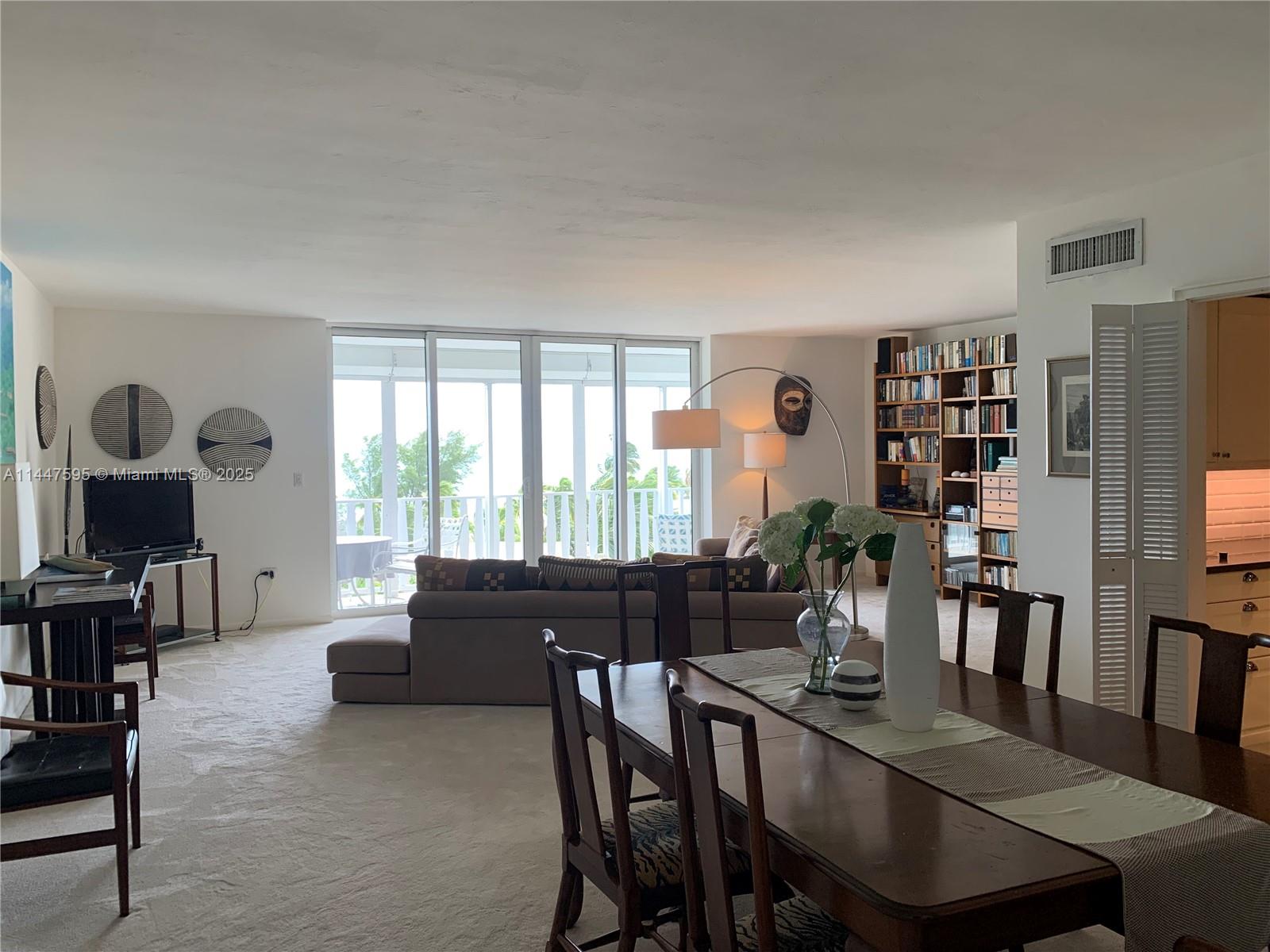 A living and dining area features a beige sectional, wooden bookshelf, and floor-to-ceiling balcony windows — 200 Ocean Lane Dr # 706, Key Biscayne FL 33149, KEY BISCAYNE, FL