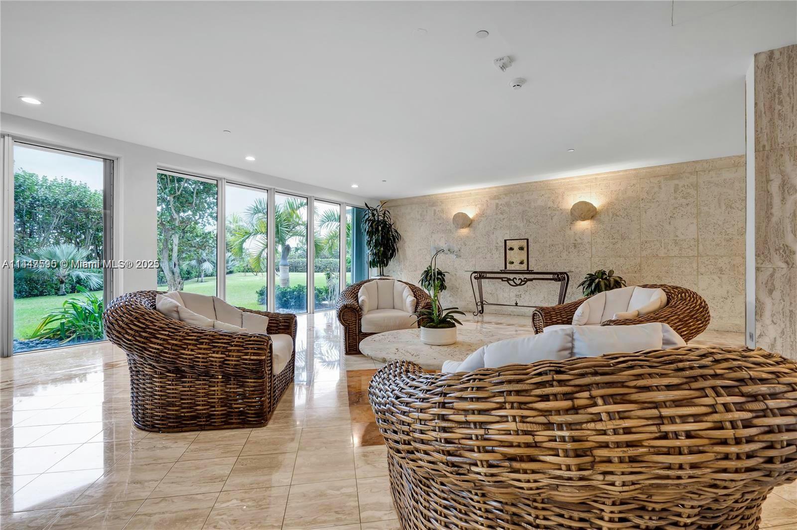 A sunlit living room features wicker furniture, marble floors, and floor-to-ceiling windows overlooking greenery — 200 Ocean Lane Dr # 706, Key Biscayne FL 33149, KEY BISCAYNE, FL