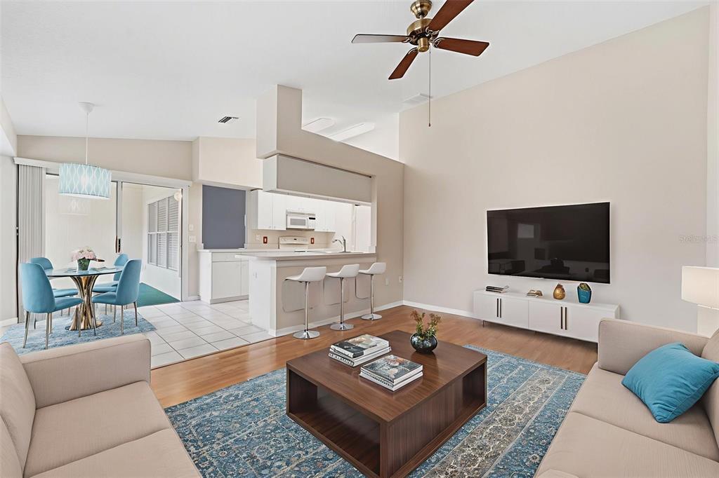 A living room with wood floors, a ceiling fan, and an open kitchen with bar seating — 1031 ALMONDWOOD DRIVE, TRINITY, FL