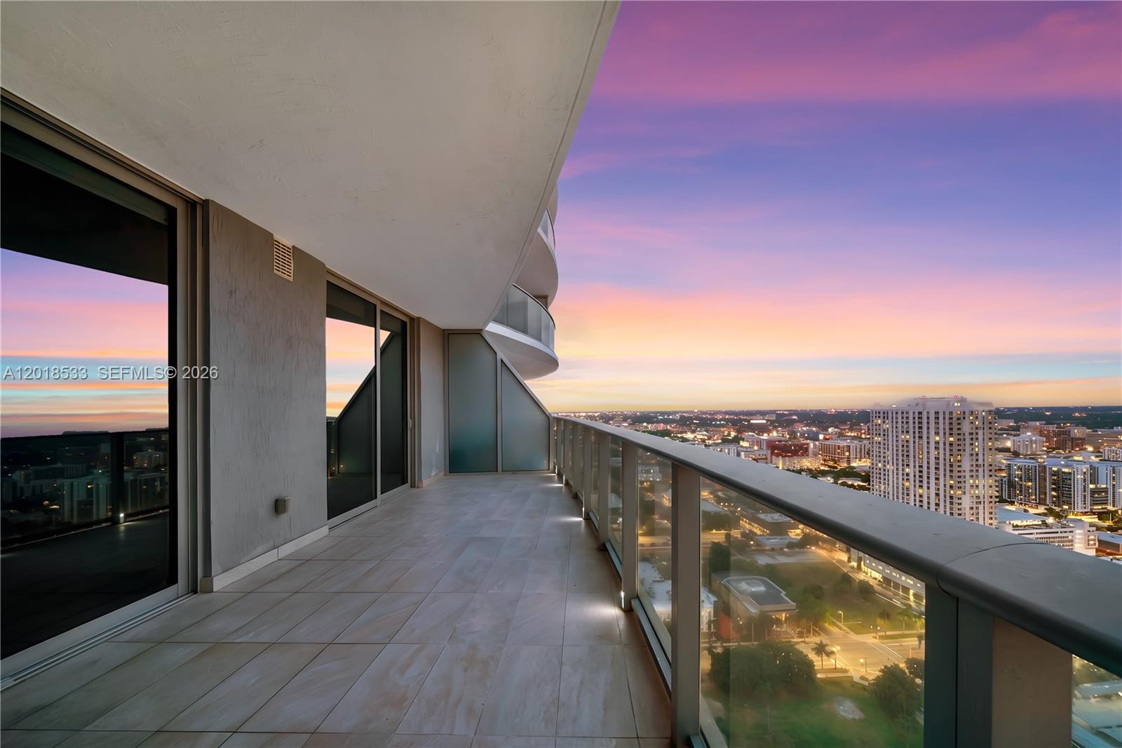 A high-rise balcony features tiled flooring, a glass railing, and panoramic city sunset views — 488 NE 18th St # 4005, Miami FL 33132, MIAMI, FL