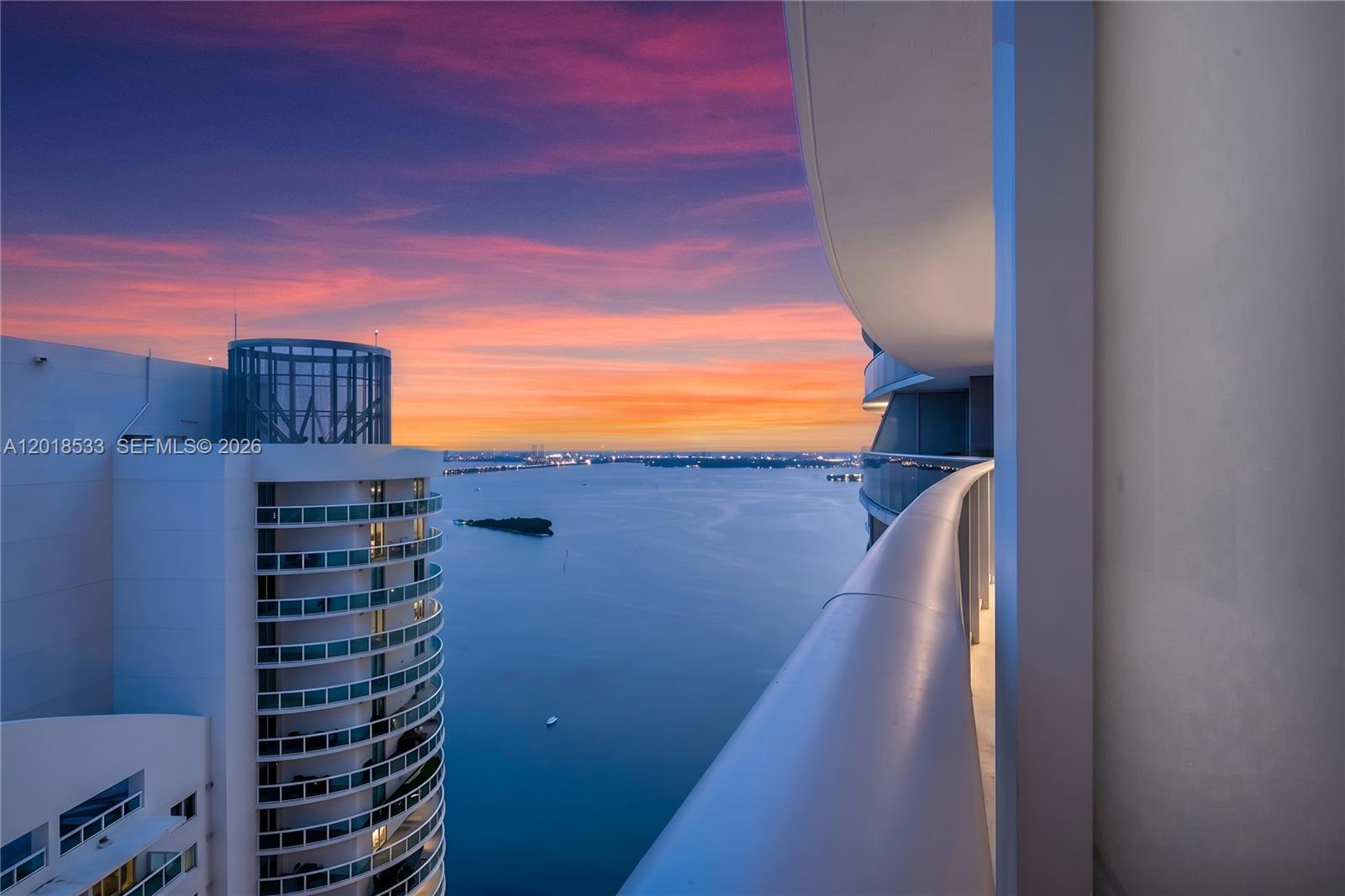 A high-rise balcony overlooks a bay and a neighboring circular building at sunset — 488 NE 18th St # 4005, Miami FL 33132, MIAMI, FL