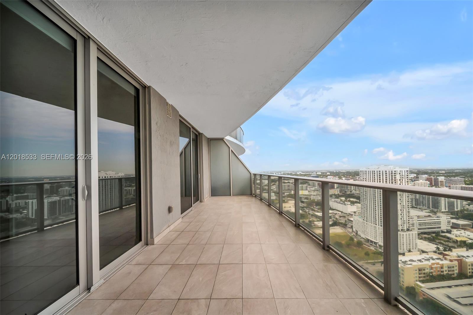 A spacious high-rise balcony features tiled flooring, glass railings, and expansive city views — 488 NE 18th St # 4005, Miami FL 33132, MIAMI, FL