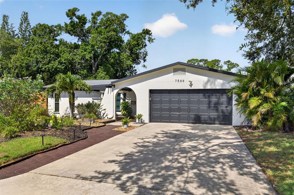 A single-story house with a white stucco exterior, dark garage door, and a concrete driveway — 7566 20TH STREET N, ST PETERSBURG, FL