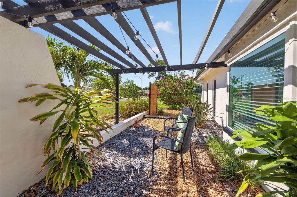 A patio with a wooden pergola, gravel ground, and two chairs beside a house exterior — 7566 20TH STREET N, ST PETERSBURG, FL