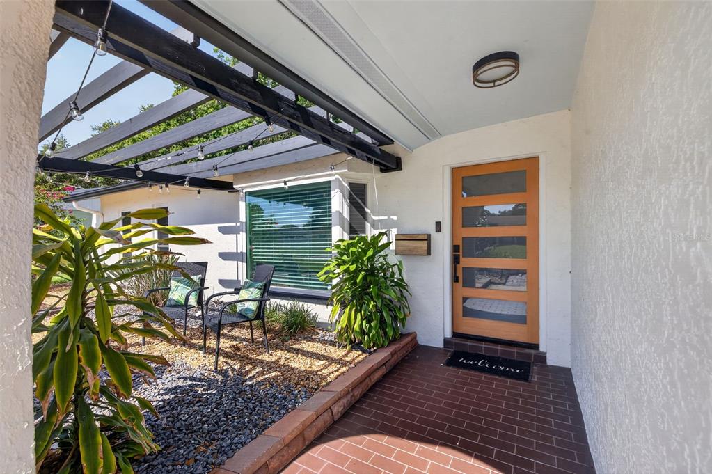 A front porch features a wooden door, a pergola, and a gravel seating area — 7566 20TH STREET N, ST PETERSBURG, FL