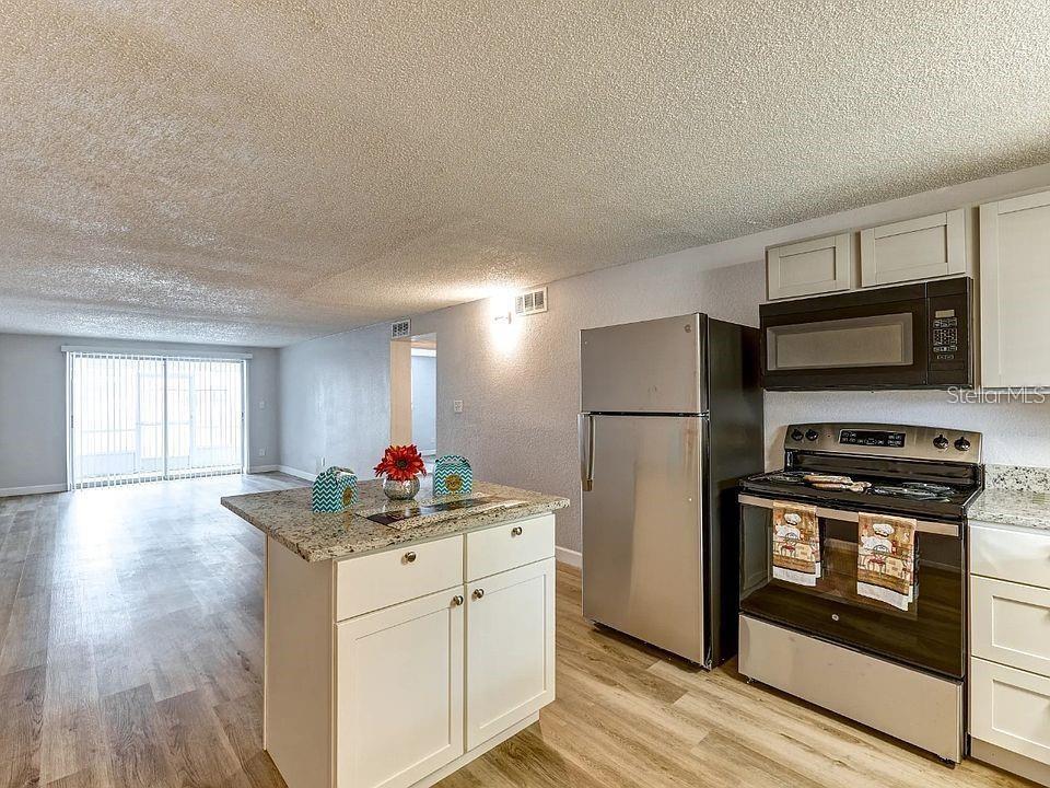 A kitchen with a granite-topped island and stainless steel appliances opens to a living area — 9901 AQUARIUS DRIVE UNIT 8, PORT RICHEY, FL