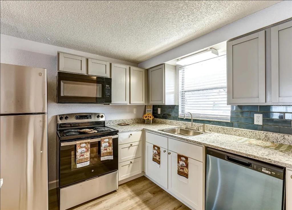 A kitchen features stainless steel appliances, light-colored cabinets, granite countertops, and a dark tile backsplash — 9901 AQUARIUS DRIVE UNIT 8, PORT RICHEY, FL