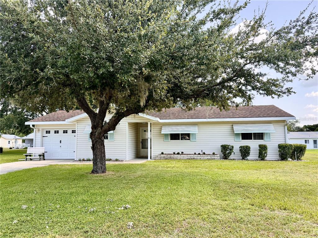 A single-story house with light siding, a garage, and a large tree in the front yard — 17929 SE 105TH AVENUE, SUMMERFIELD, FL