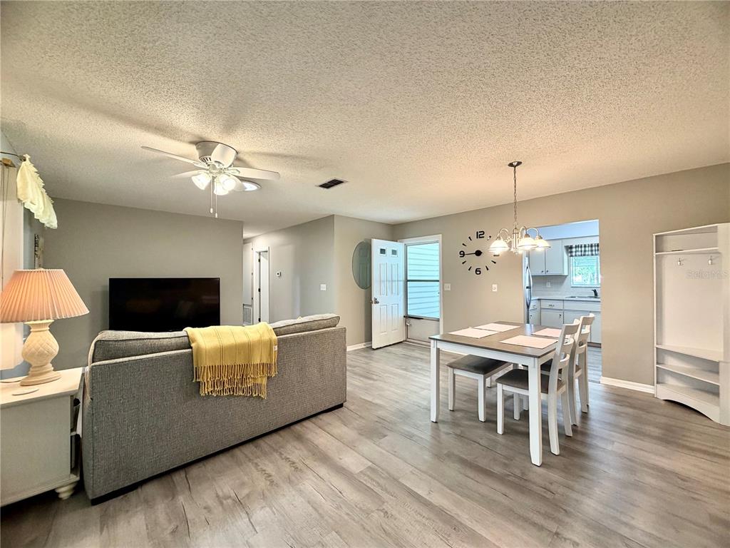 A living and dining area with gray wood-look flooring, a gray sofa, and sliding doors — 17929 SE 105TH AVENUE, SUMMERFIELD, FL