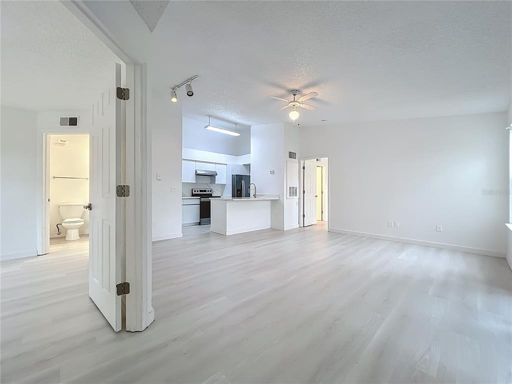 An open-concept living area features light wood-look flooring, a kitchen with white cabinets, and a bathroom — 2225 METROPOLITAN WAY UNIT 1225, ORLANDO, FL