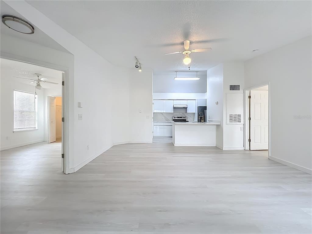 A bright, open-concept living area features light wood-look flooring and a view into the kitchen — 2225 METROPOLITAN WAY UNIT 1225, ORLANDO, FL