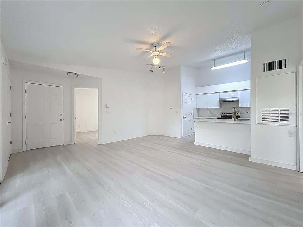 An open-concept living area features light wood-look flooring, white walls, and an adjacent kitchen — 2225 METROPOLITAN WAY UNIT 1225, ORLANDO, FL
