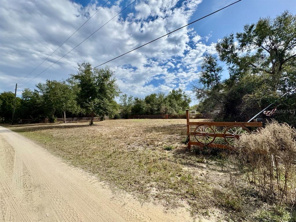 A dirt road runs alongside a vacant, grassy lot with a decorative wooden wagon-wheel gate — NE 135TH STREET, SALT SPRINGS, FL
