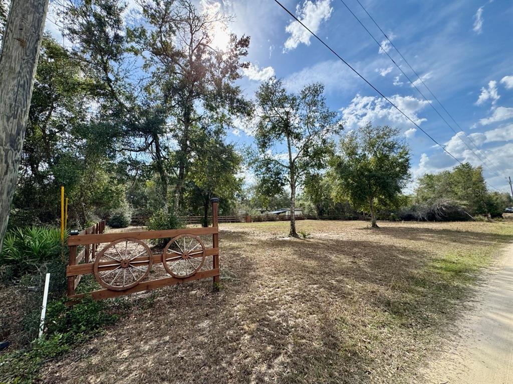 A wooden fence with decorative wagon wheels borders a grassy, tree-filled lot under a sunny sky — NE 135TH STREET, SALT SPRINGS, FL