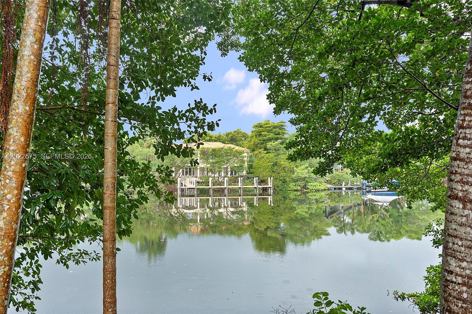A wooden dock extends into a calm canal surrounded by lush trees and a house — 7244 E Lago Dr, Coral Gables FL 33143, CORAL GABLES, FL