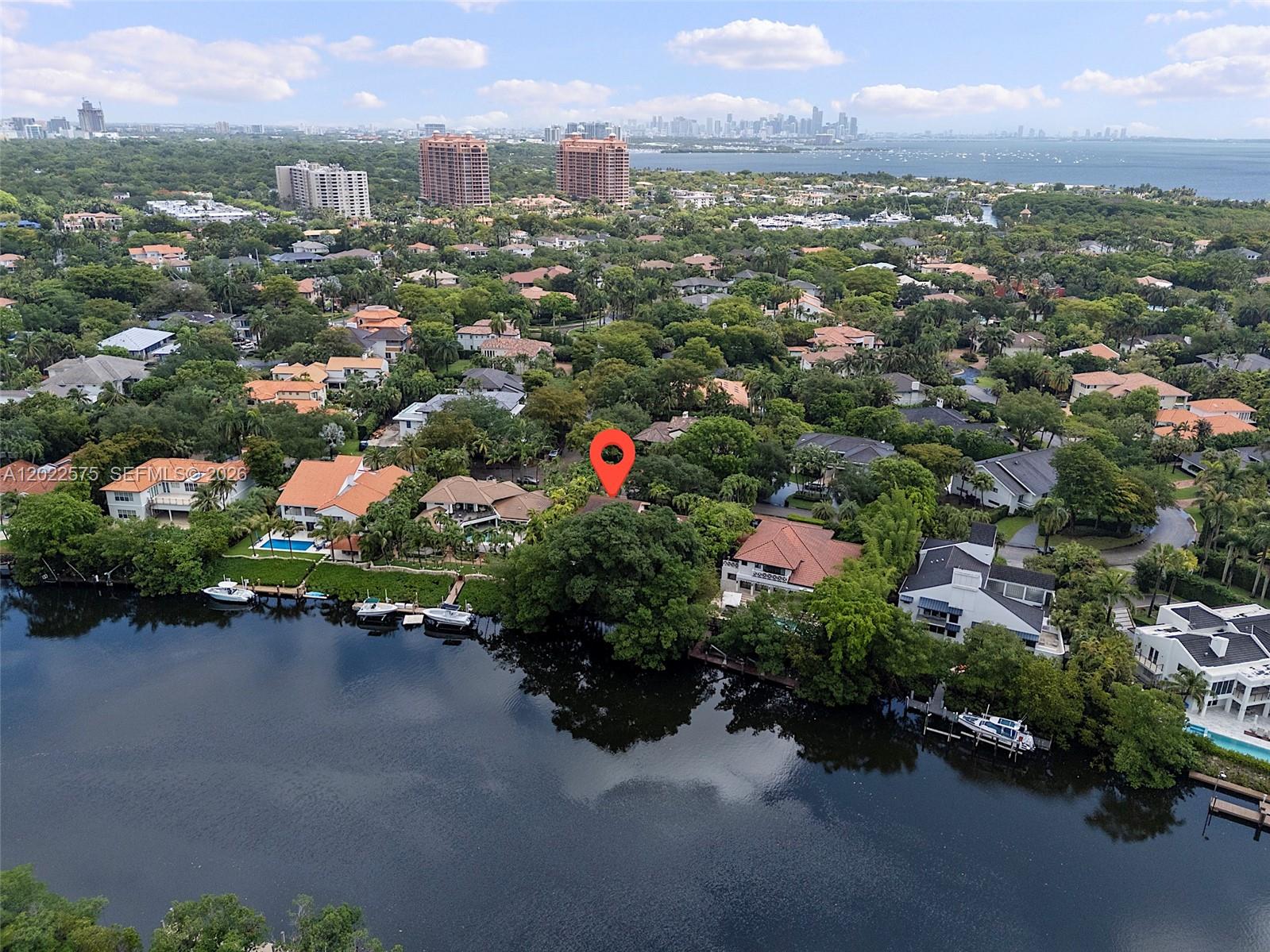 An aerial view shows waterfront homes surrounded by dense trees with a city skyline backdrop — 7244 E Lago Dr, Coral Gables FL 33143, CORAL GABLES, FL