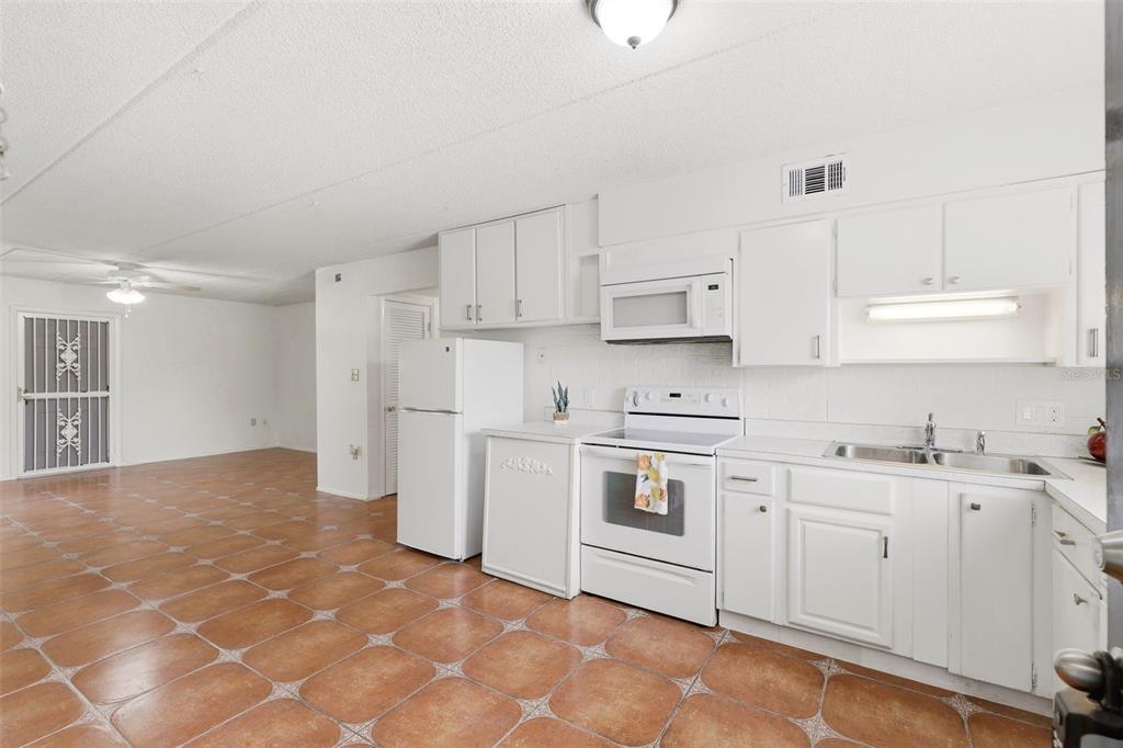 A kitchen with white cabinets and appliances features brown tiled flooring and an adjacent room — 525 CONWAY ROAD UNIT 29, ORLANDO, FL