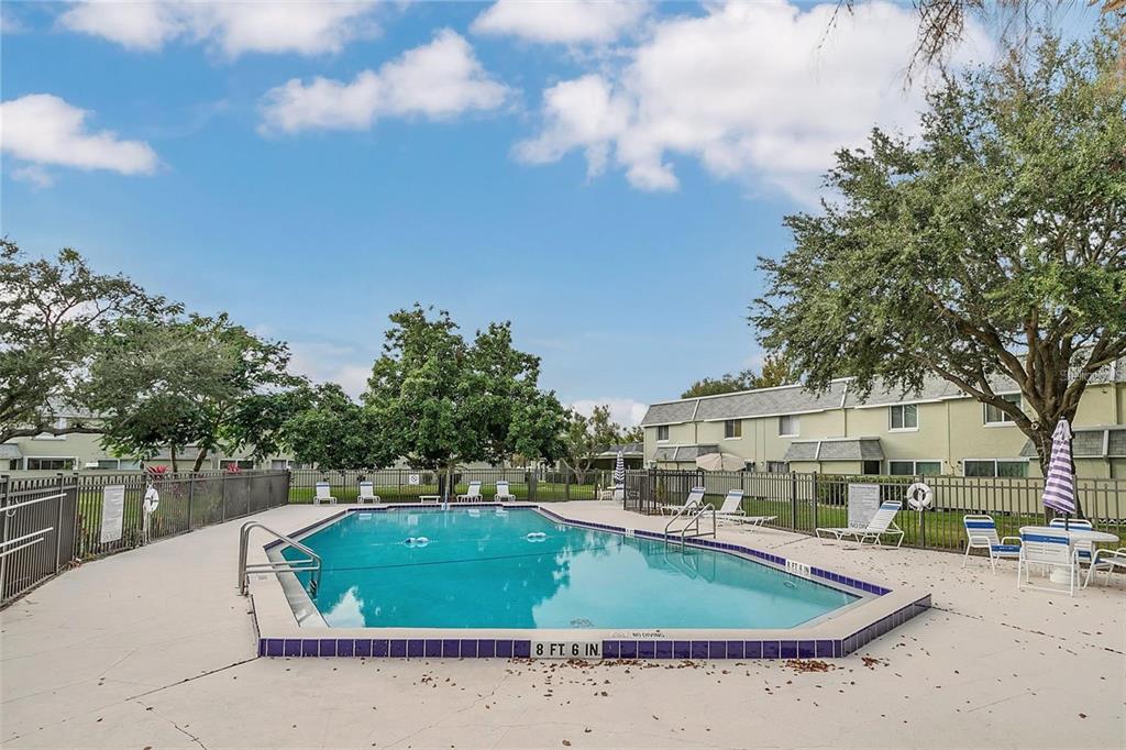 A rectangular swimming pool is surrounded by a concrete deck, metal fencing, and apartment buildings — 525 CONWAY ROAD UNIT 29, ORLANDO, FL