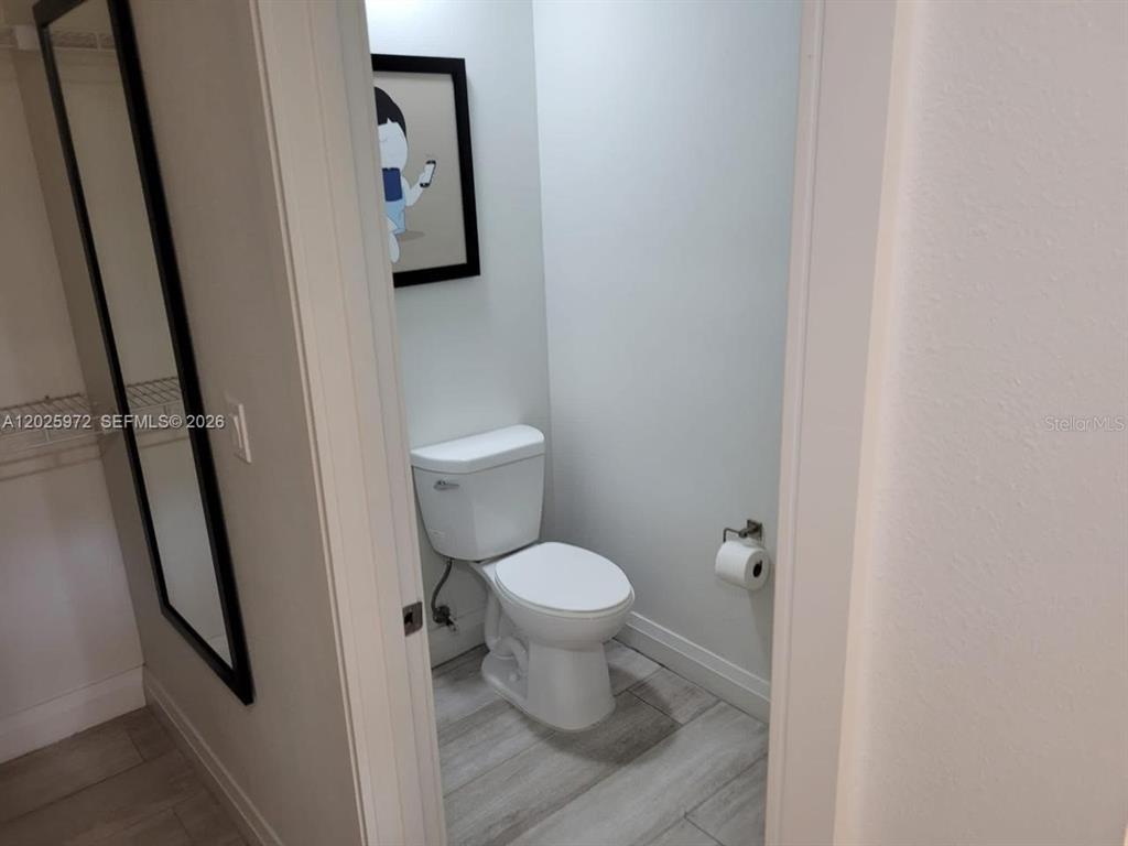 A small bathroom features a white toilet, light wood-look tile flooring, and a framed wall art — 14501 GROVE RESORT AVENUE UNIT 3425, WINTER GARDEN, FL