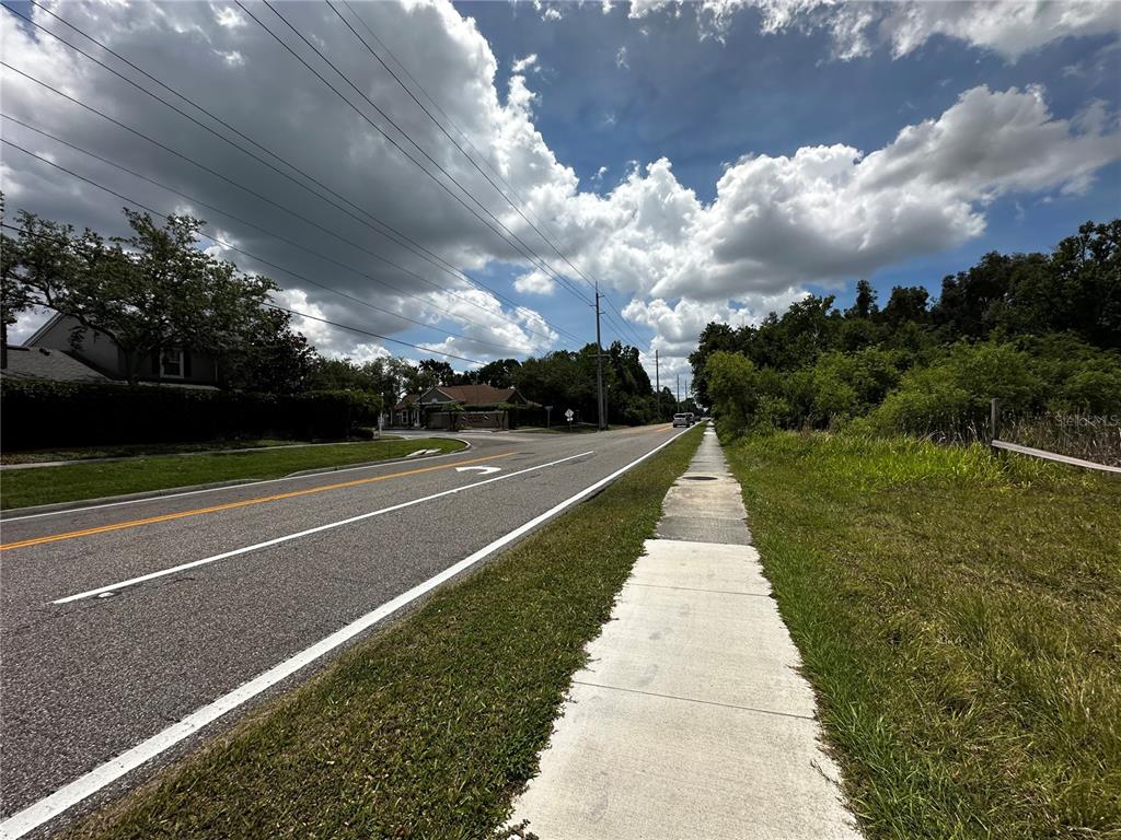 A paved road with a sidewalk runs alongside a grassy area under a cloudy sky — 11580 HENDERSON ROAD, TAMPA, FL