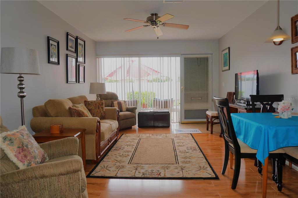 A living and dining area with hardwood floors, a ceiling fan, and a sliding glass door — 4337 TAHITIAN GARDENS CIRCLE UNIT F, HOLIDAY, FL