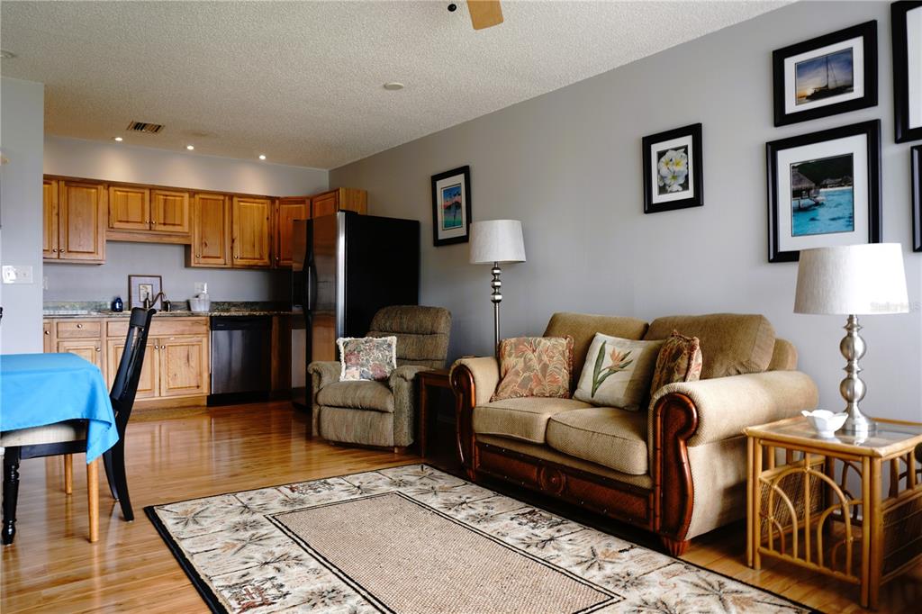 A living room with a sofa and armchair sits adjacent to a kitchen with wooden cabinets — 4337 TAHITIAN GARDENS CIRCLE UNIT F, HOLIDAY, FL