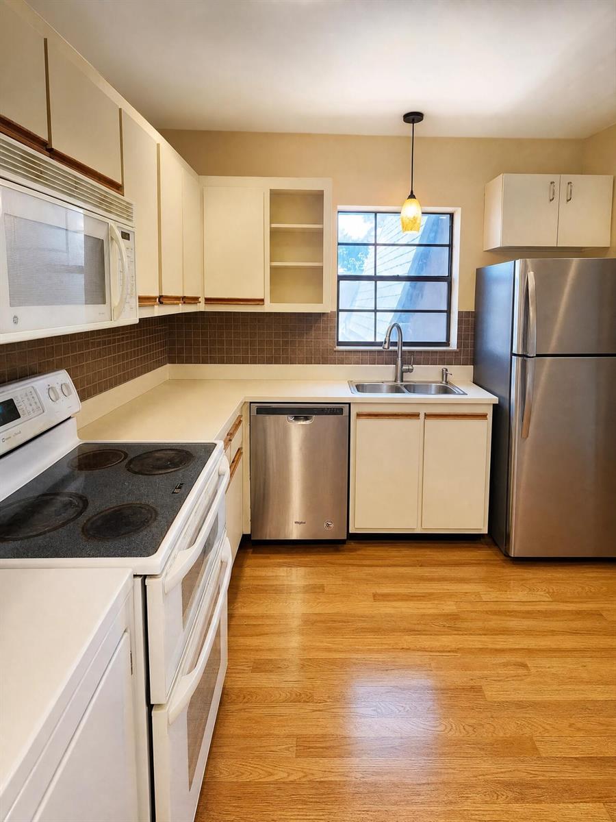 A kitchen features white cabinets, stainless steel appliances, a tiled backsplash, and light wood flooring — 3575 NW 94th Avenue # 8d, Sunrise FL 33351, SUNRISE, FL