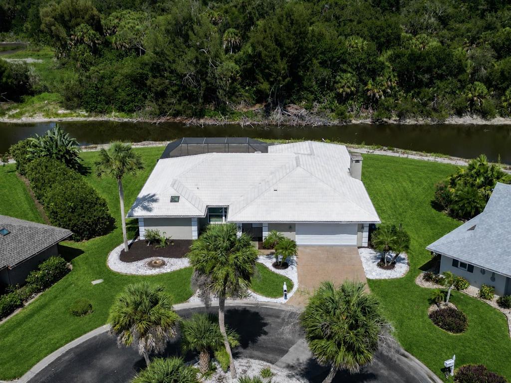 An aerial view of a suburban house with a white roof, pool cage, and waterfront backyard — 1130 MISTI COURT, VENICE, FL