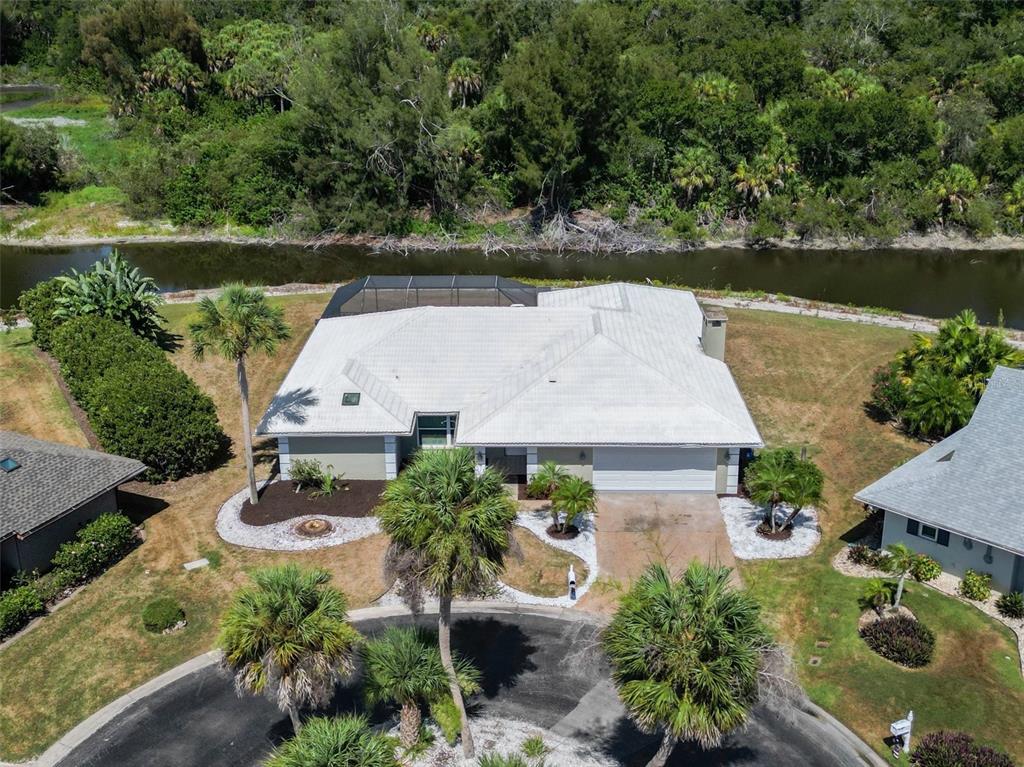 An aerial view shows a single-story house with a white roof, pool cage, and canal — 1130 MISTI COURT, VENICE, FL