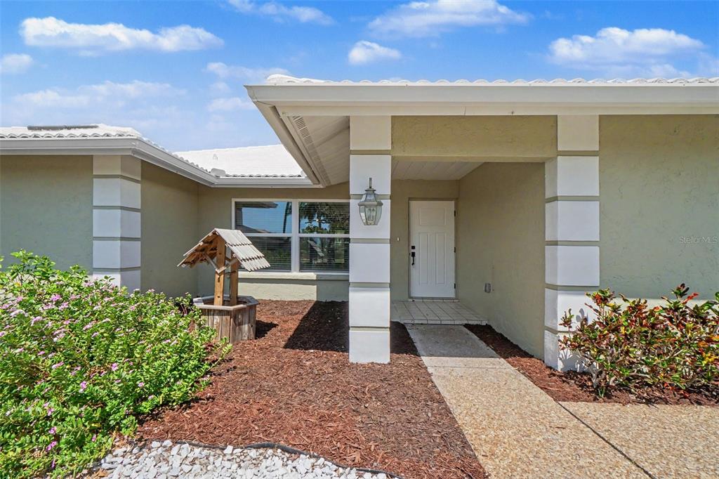 The exterior of a house features a white front door, a wishing well, and landscaping — 1130 MISTI COURT, VENICE, FL
